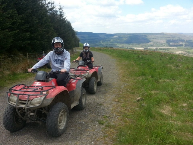  Dos niños con cascos blancos, sonriendo y a punto de manejar quads rojos por el bosque 