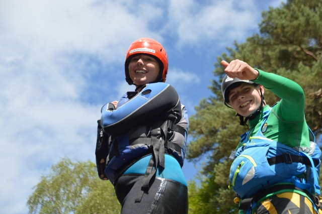  Dos niños sonriendo vistiendo trajes de baño azul y verde mientras hacen barranquismo