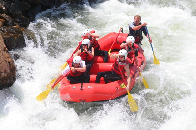  Personas con casco blanco y chalecos rojos ayudas a la flotabilidad haciendo carrera de rafting