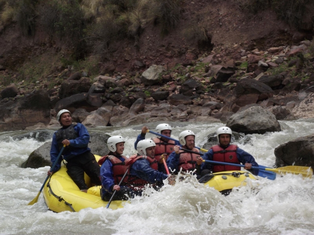  Personas con casco blanco y chalecos salvavidas rojos haciendo una carrera de rafting 