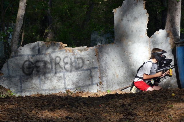 Niño con playera gris y rojo pantalones cortos jugando paintball