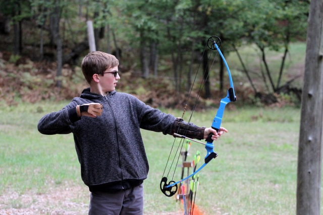  Niño con lentes de sol y suéter gris haciendo jalo con arco 