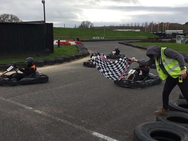  5 personas con cascos negros y trajes de conducción duranle una carrera de karting 