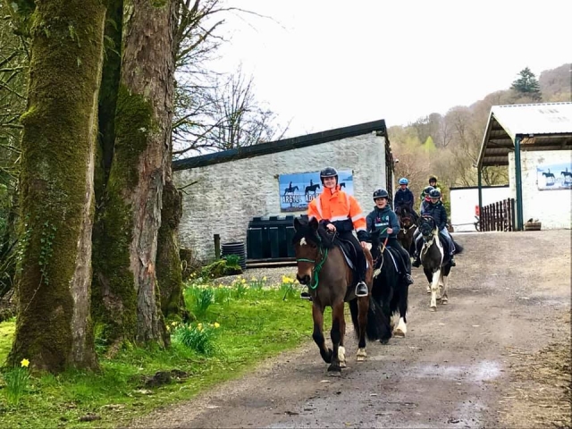  Instructor vestido de negro casco y chamarra naranja con niños subiendo a caballo