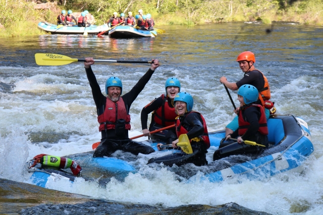  Genle sonriendo y pasándola bien, con casco azul y chalecos salvavidas rojos duranle la sesión de rafting 