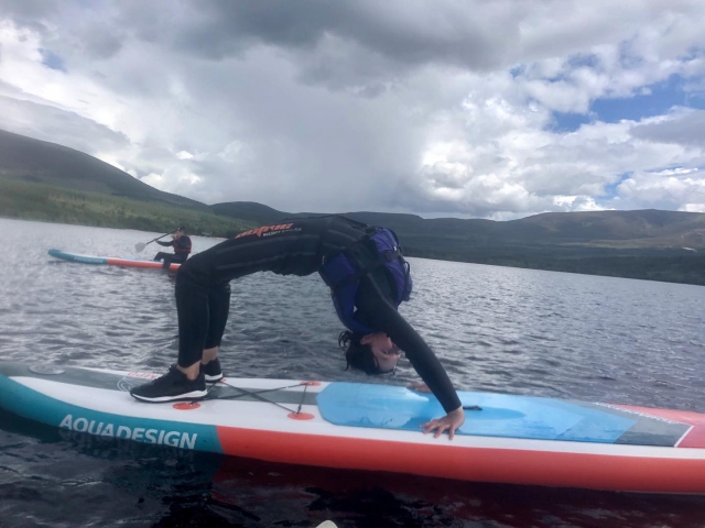  Niña haciendo yoga, usando ayudas a la flotabilidad azules duranle su sesión de paddleboard
