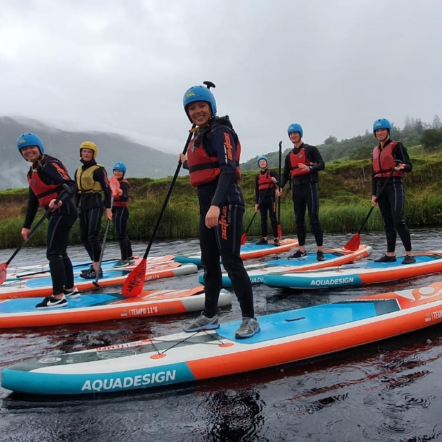  Personas con cascos azules y ayudas a la flotabilidad rojas sonriendo mientras practican paddleboarding 