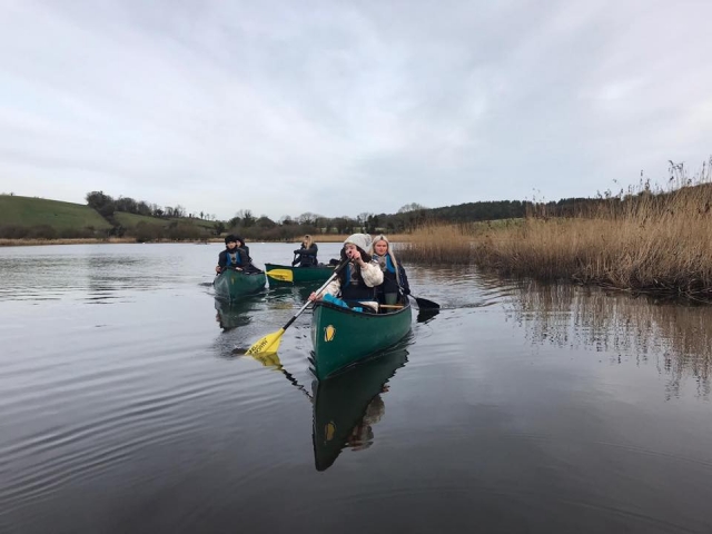  Niñas con ayudas de flotabilidad negras en canoas verdes haciendo piragüismo en tándem en el lago