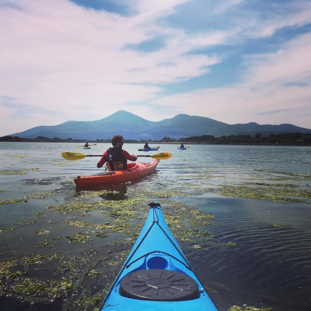  Personas con trajes de neopreno rojos navegando en el lago en canoas rojas y azules 