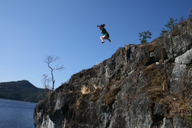  Chica con playera verde saltando desde un acantilado mientras practica coasteering 