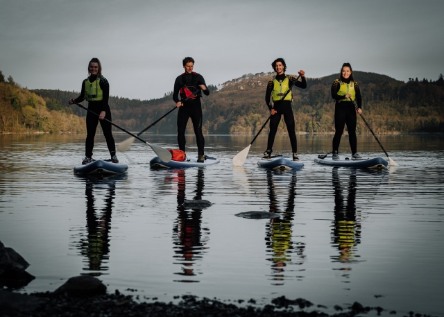  Cuatro personas con trajes de neopreno negros, ayudas a la flotabilidad verdes surf de remo en el lago 
