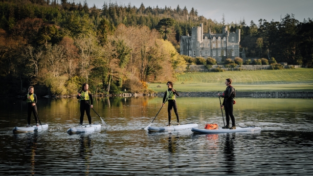  Grupo de 5 amigos usando chalecos salvavidas verdes y haciendo paddle board en el lago