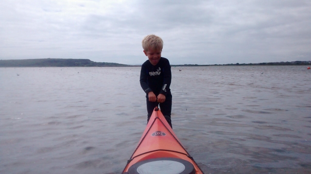  Niño jalando del kayak rojo hacia el mar para empezar su sesión de kayak 
