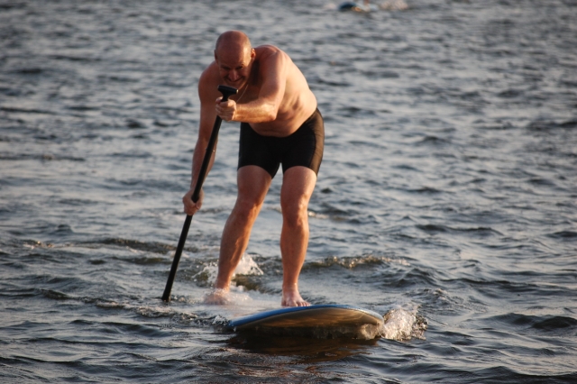  Hombre en traje de baño negro sonriendo mientras hace paddleboarding 