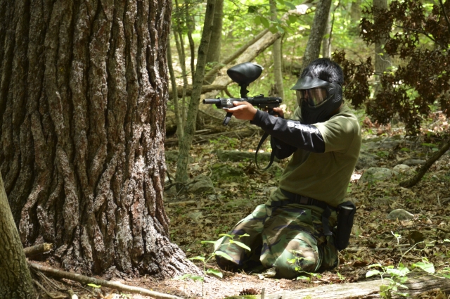  Hombre de rodillas jugando gotcha y vestido con traje de camuflaje 