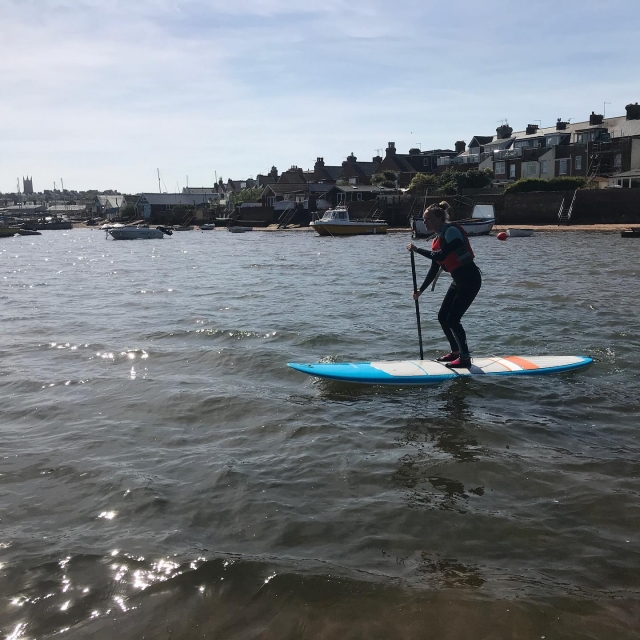 Chica chavo en paddleboard azul haciendo paddleboard en el río camello