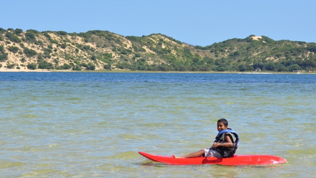 Chico en kayak rojo y vistiendo ayudas a la flotabilidad azul practicando kayak