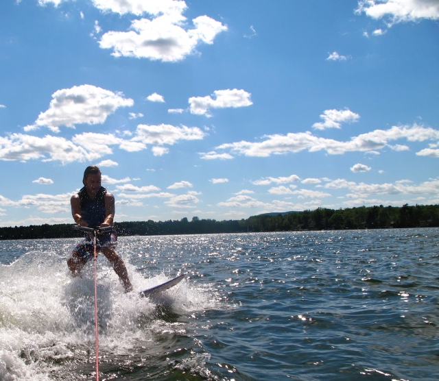Niño con ayudas a la flotabilidad negras y azules haciendo wake surf