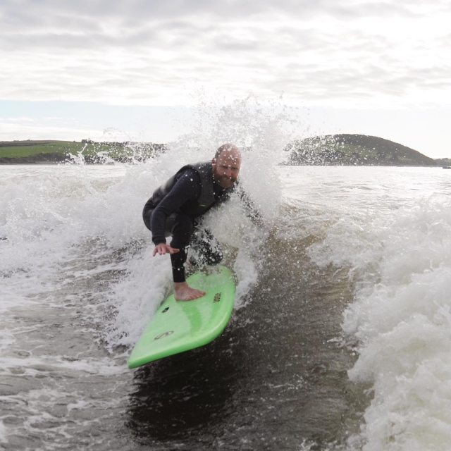 Hombre haciendo wake surf sobre un barco de surf verde
