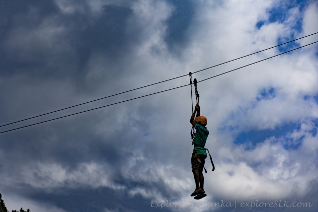  Niño con playera verde y casco naranja en el aire mientras realiza su sesión de tirolesa 