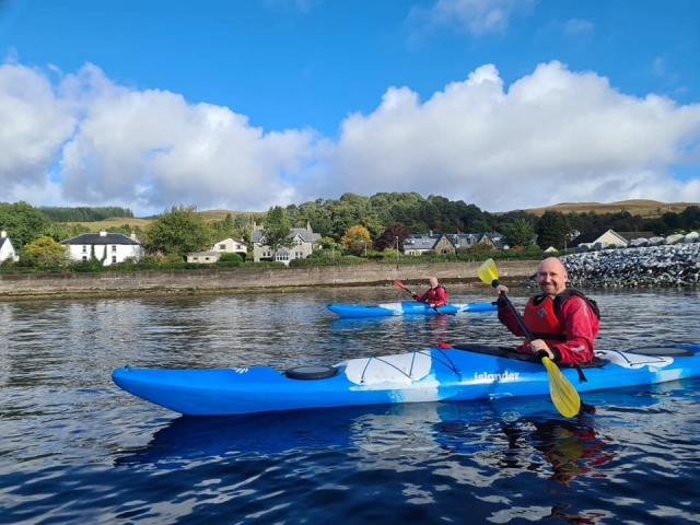 Dos hombres con ayudas a la flotabilidad rojas en kayaks azules