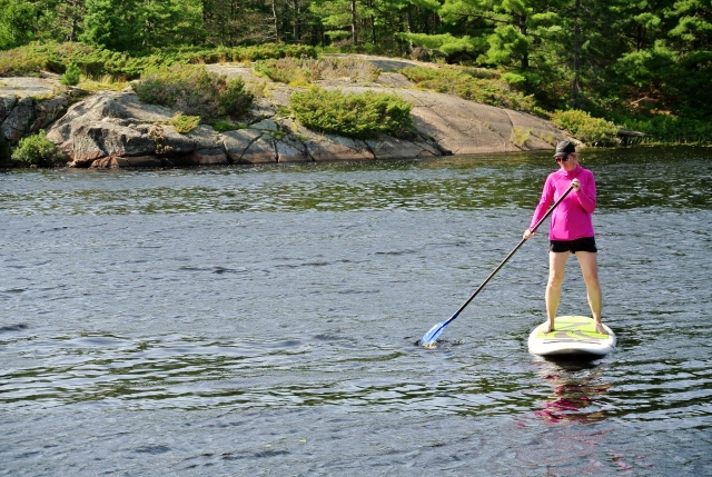 Mujer con chamarra rosa y gorra haciendo remo en paddleboard blanco
