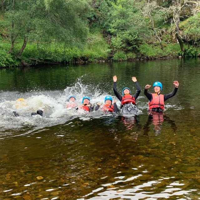 Amigos con flotadores rojos ayudantes y cascos azules haciendo la ola duranle su sesión de barranquismo