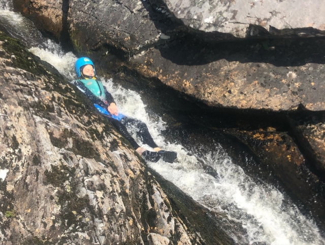 Niña con casco azul y chalecos salvavidas azules saltando de una cascada duranle su sesión de descenso de cañones