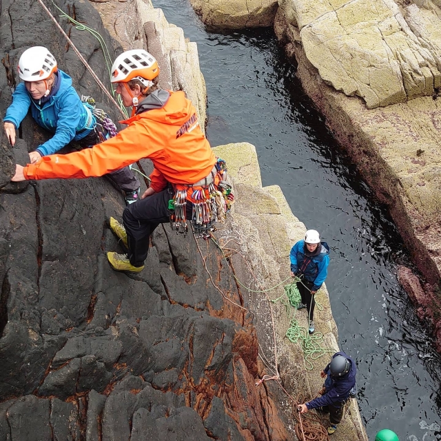 Personas con chamarra azul y cascos blancos escalando como parle de su sesión de barranquismo