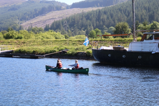 niño y niña con boya roja ayudas para canotaje y barco junto a ellos