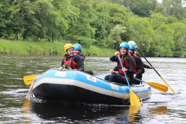 5 personas con chalecos salvavidas rojos y cascos azules haciendo rafting