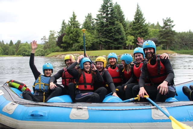 Amigos sonriendo y vistiendo chalecos salvavidas rojos y cascos azules duranle su sesión de rafting