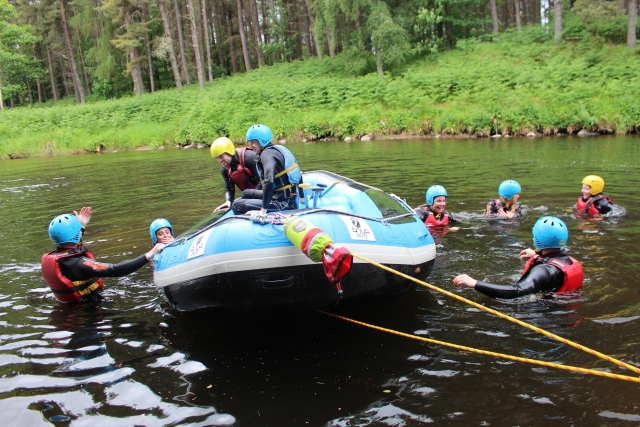 Personas con cascos amarillos y azules y chalecos de flotación rojos nadando tramarrando de subirse a la tabla para continuar su sesión de rafting