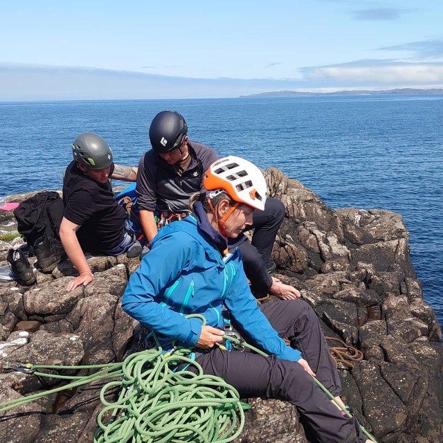 Tres personas en la cima de la colina vestidas de blanco y negro cascos y ayudar a otro cuale a escalar y alcanzarlos