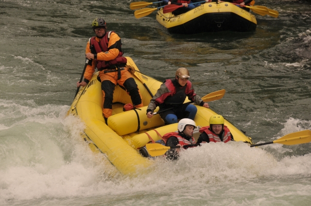  Personas con cascos negros y azules, chalecos salvavidas naranjas, trajes de neopreno rojos y rafting en bole amarillo 