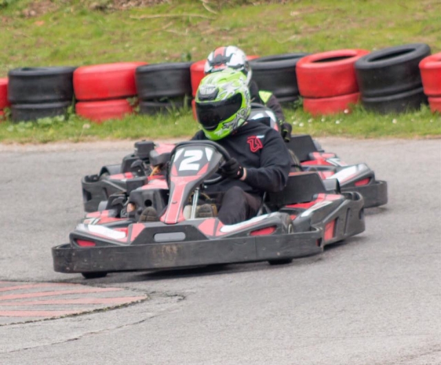 Chavos con cascos verdes y azules, trajes negros y guantes negros mientras practican karting