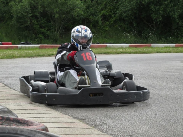 Conductor con traje de conducción negro y casco azul divirtiéndose practicando karting