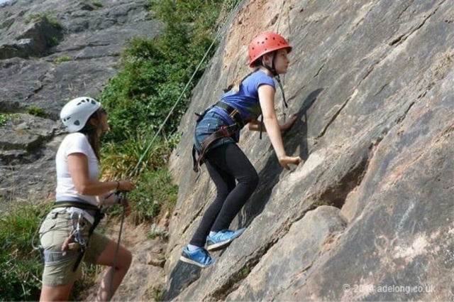  Niña con casco rojo mientras escala en roca con su madre, vestida de blanco 