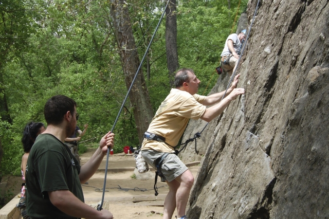  Hombre con playera amarilla preparándose para la escalada en roca con la ayuda de su familia y el instructor