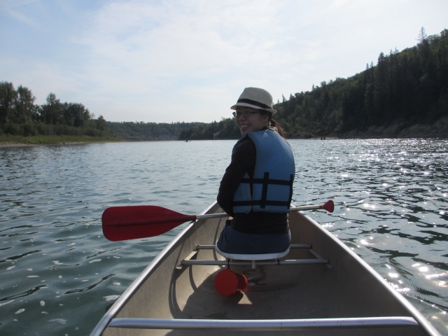 Mujer con sombrero y ayudas de flotabilidad azules mientras navega en canoa 