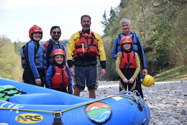 Familia feliz con cascos rojos y ayudas de flotabilidad azules preparándose para hacer piragüismo