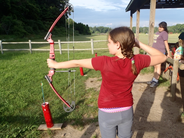  Chica con playera roja con su madre detrás practicando jalo con arco por primera vez 