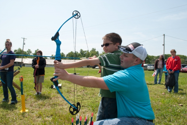  Niño con playera verde y lentes de sol practicando jalo con arco 