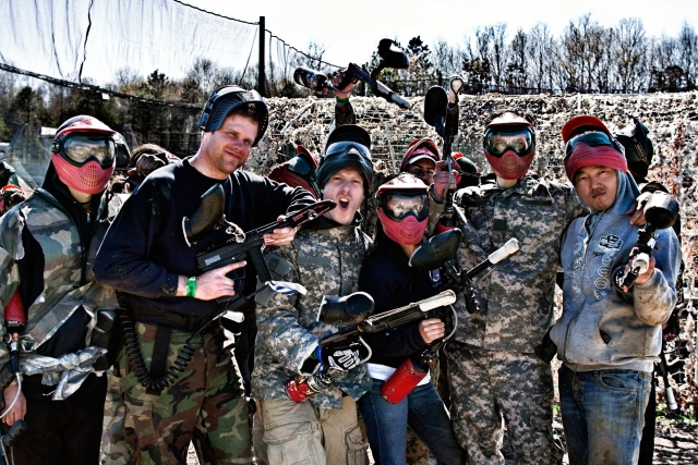  Grupo de 6 amigos con trajes negros y de camuflaje divirtiéndose después de su sesión de paintball
