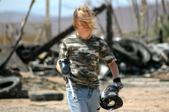 Chica con playera de camuflaje y jeans quitándose la máscara después de jugar gotcha 
