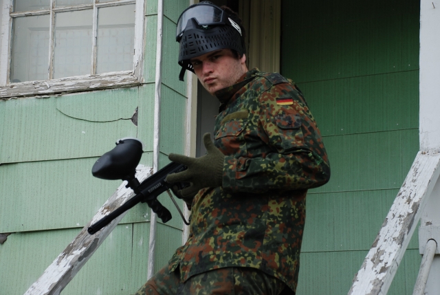 Niño con traje de camuflaje y máscara negra a punto de jugar paintball