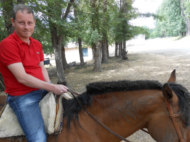  Hombre sonriendo con playera roja y subiendo un caballo marrón 