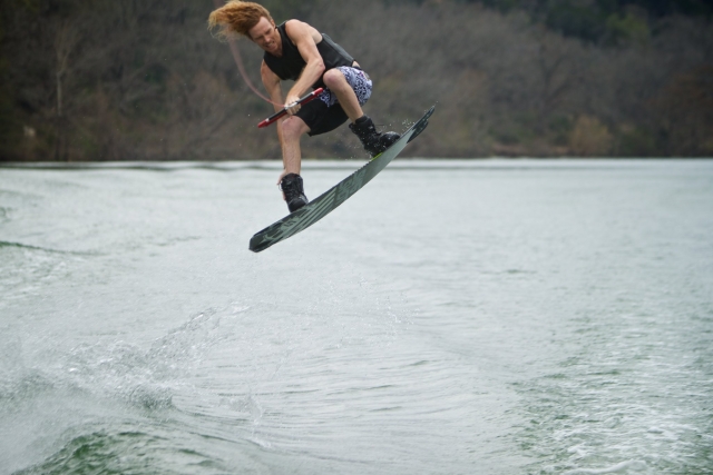  Niño con ayudas de flotabilidad negras saltando una ola mientras hace wakeboard 