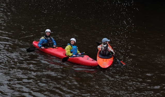 Pareja con ayudas de flotabilidad azules y casco en un kayak rojo haciendo nuestro kayak en tándem 