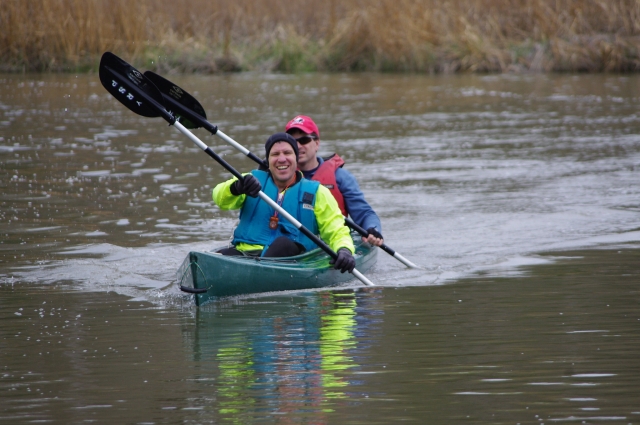  Pareja sonriendo, usando ayudas de flotabilidad azules en un kayak en tándem verde 